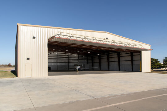 Small jet inside beige metal aircraft hangar on clear sunny day