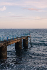 Fototapeta premium Concrete pier with blue railings over the ocean at sunset