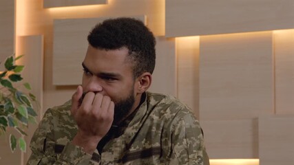 Portrait of worried uncertain black male army soldier in military uniform nail biting, expressing anxiety and tension while visiting counsellor during psychotherapy session office.