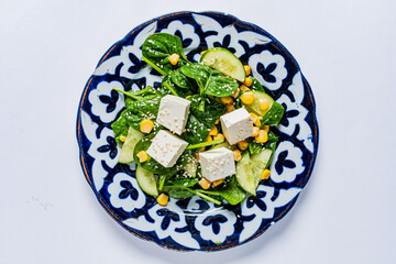 A colorful salad features fresh spinach, crisp cucumbers, sweet corn, and tofu cubes