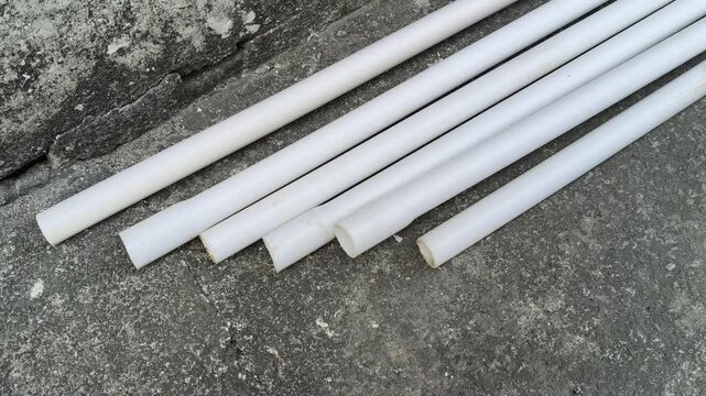 Electrical PVC pipes. White, rigid plastic pipes are laid on an old, gray concrete surface next to a textured wall. These pipes are used for electrical wiring.