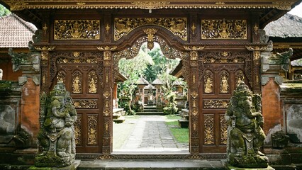 Fototapeta premium Ancient balinese gate with intricate carving and traditional stone statue leading to a lush temple courtyard. Culture, religion, and tourism.