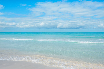 Fototapeta premium Calm ocean waves gently lap on the sandy shore under a bright blue sky