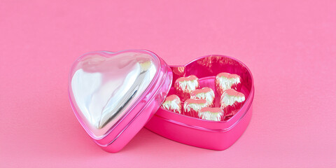 Heart-shaped gift box filled with chocolates on pink background