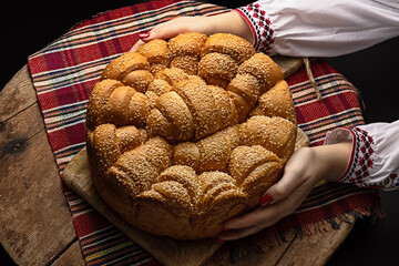 Festive artisan homemade round bread and hands of bulgarian woman in traditional ethnic costume with folklore embroidery. Culture and food in Bulgaria
