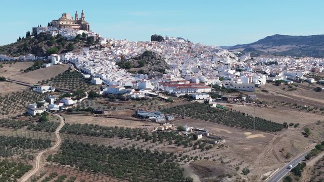 Aerial drone shot panorama wide view of the white town village of Olvera in Andalusia, Spain, Europe. Traditional castle and church on hill, and olive trees. Drone orbiting. Cinematic grading