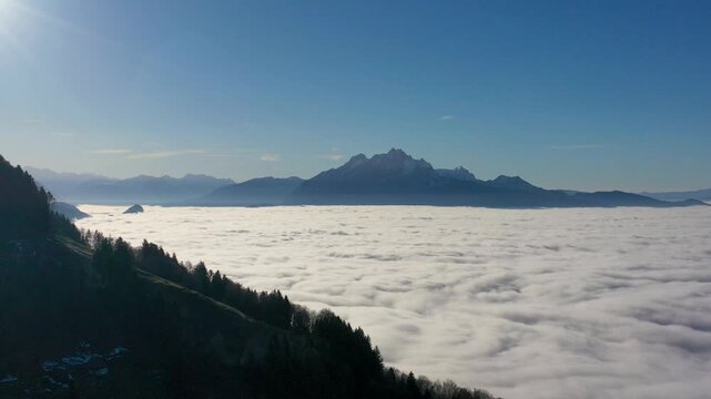 Drone pans left-to-right above Nebelmeer fog layer inversion phenomena revealing group of Alpine peaks with Pilatus massif anchoring panorama above stratus clouds near Geneve, Central Switzerland