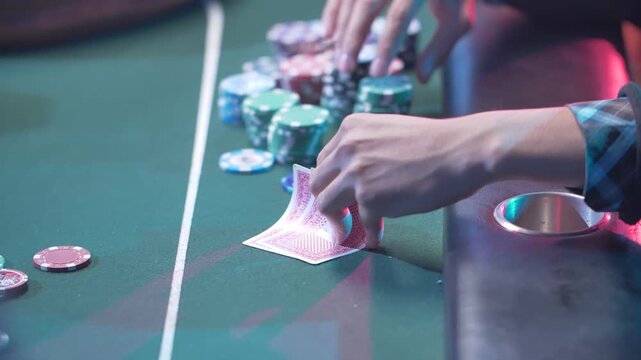 Cinematic close up of a player's hands checking two hole cards next to a large stack of poker chips on a green felt table in a luxury casino.