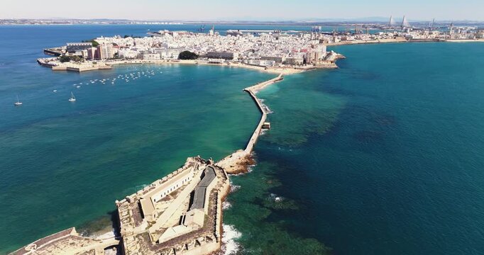 Beautiful cinematic aerial drone cityscape shot of C&aacute;diz in Spain, Andalusia, Europe, on bright sunny day, facing La Caleta beach and Cadiz city waterfront. Cinematic dark grading