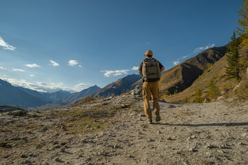 Hiker with backpack walks on mountain trail. Scenic Altai valley with blue sky background. Adventure, travel, freedom, nature.