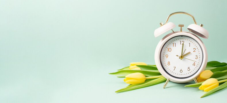 Alarm clock with yellow tulip flowers, switch to daylight saving time in spring, summer time changeover