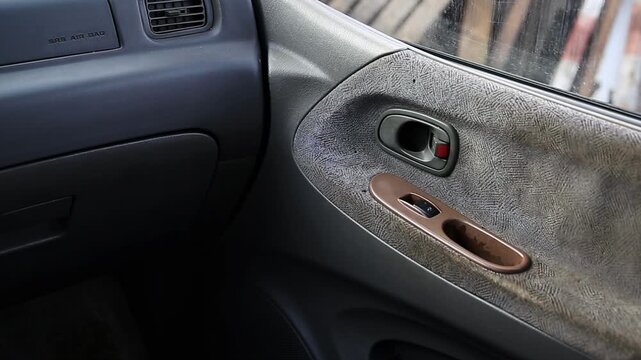 Car interior passenger side. Door panel detail: handle, window switch, worn fabric. Dashboard air vent, SRS AIR BAG label. Aged car.