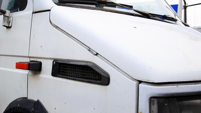 Detail view of old white commercial van front right side. Hood slightly open. Exterior shows dirt, grime, rust. Signs of age, heavy commercial use. Orange side marker light on plain body.