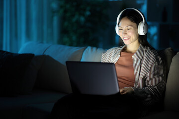 Happy asian woman wearing headphone in the night using laptop