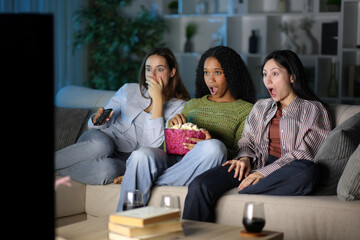 Amazed friends watching tv program at home in the night
