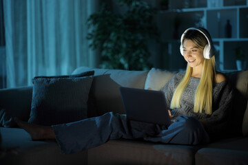 Happy woman wearing headphone using computer in the night