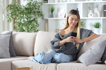 Relaxed woman at home using smart phone seated on a couch