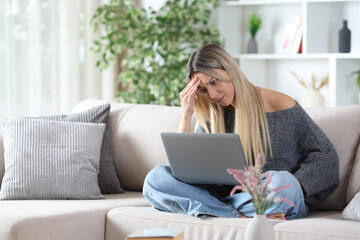 Worried woman on a sofa checking personal computer