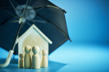 Family security concept wood figurine and model house under umbrella.