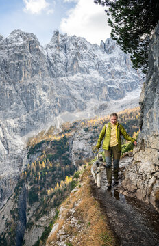 Woman hiking with dog on narrow mountain trail in the Dolomites