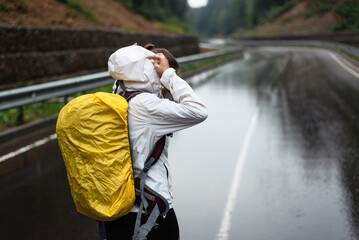 Backpacker in rain adjusting hood on wet road with yellow backpack