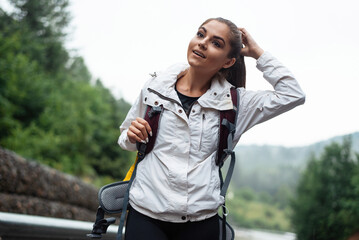 Hiker with backpack pauses on a misty mountain road, touching her hair