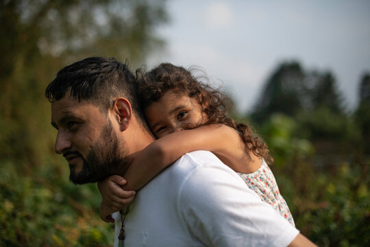 Hispanic father giving young daughter a piggyback ride outside