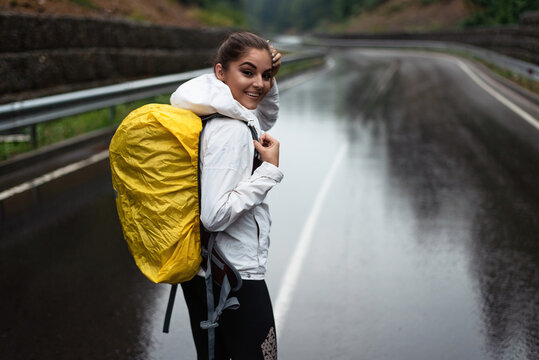 Girl with a yellow backpack on a wet road, smiling at the camera
