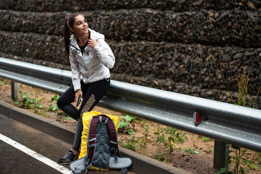 Girl in sportswear resting by the roadside with a backpack and phone