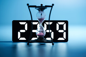 focus on background , midnight 23:59 digital clock with hourglass countdown on blue background