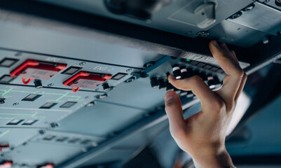 Close-up of pilot hand adjusting switches on overhead aircraft panel