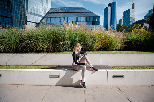 Girl in athletic wear sitting on bench in modern city park