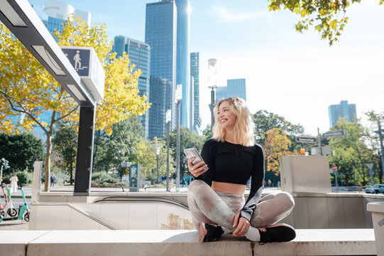 Girl with smartphone sitting outdoors with city skyscrapers