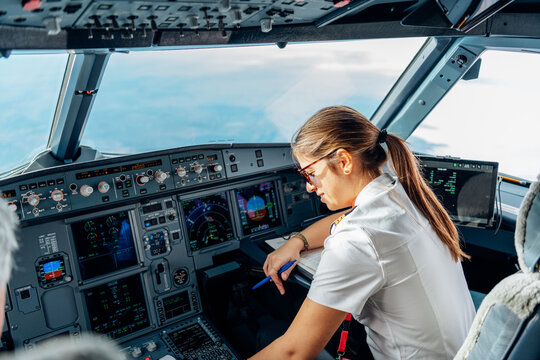 Focused female pilot writing on flight log in airplane cockpit