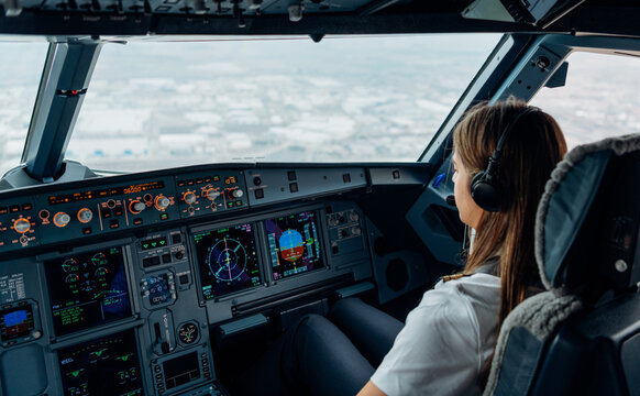 Female pilot in cockpit monitoring descent over cityscape