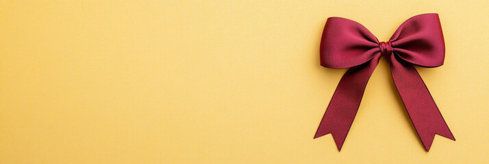 Maroon satin bow with elegant texture placed on smooth yellow background, creating festive and stylish decorative accent