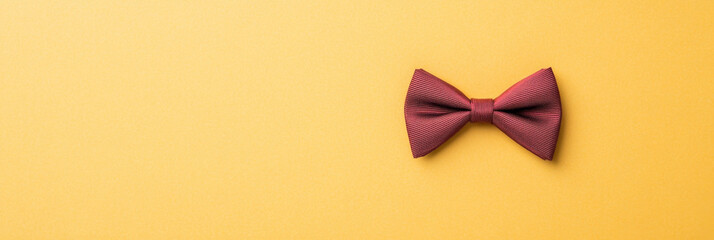 Maroon satin bow tie on yellow background, elegant accessory for formal wear, smooth texture and classic style for special occasions