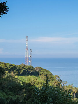 Cell Tower on Lush Green Hilltop Overlooking Blue Ocean Under Bright Sky, Offering Cellular Connectivity in Coastal Regions for Modern Communication