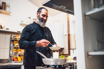 Professional chef is preparing meal in restaurant's kitchen. He makes a vegetarian lunch. He is adding food topping.