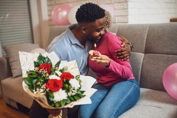 Happy loving couple celebrating woman's birthday at home. Boyfriend is giving bouquet of flowers to his girlfriend.