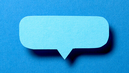 Blank cut out paper speech bubble with shadow and copy space for text on blue background, close-up flat lay top view conceptual backdrop