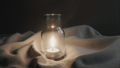 A lit candle inside a clear glass jar on a white draped surface