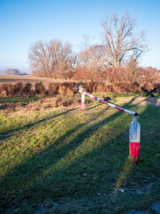 Historic border barrier with red and white metal gate arm in open field, part of former guarded border zone in Petržalka, Bratislava, Slovakia, used during the Cold War. © Marek