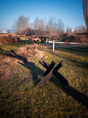 Anti-tank obstacles and border gate in an open field, part of a Cold War border zone replica in Petržalka, Bratislava, marking the former guarded boundary between East and West. © Marek