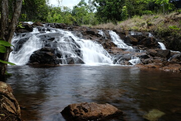 beautiful waterfall with trees and coral. water flows over dark, rugged stones, rocks creating staircase effect. The scene is serene natural landscape.