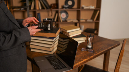 Woman in a suit using a calculator at a desk with books, laptop, and hourglass