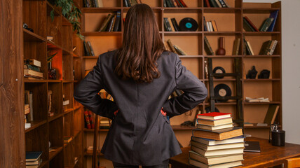 Woman in a suit standing with hands on hips in a library with bookshelves © shine.graphics
