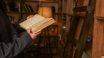 Person in a suit holding an old book in a library with bookshelves and a ladder © shine.graphics