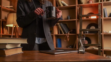 Obraz premium Person in suit holding a mug with the word WORK and glasses in a library
