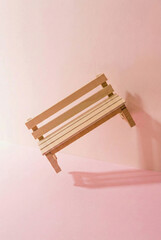 Minimalist miniature wooden bench floating against a solid pink background with aesthetic shadows.